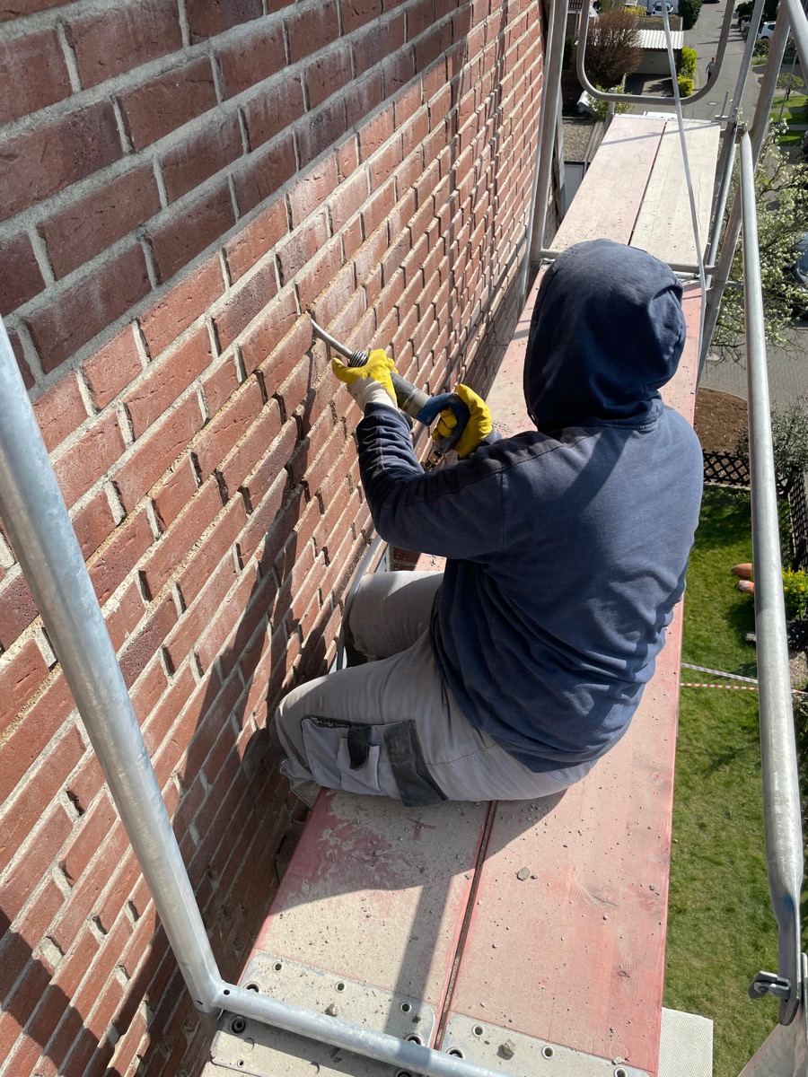 Arbeiter bei der Fugensanierung an der Klinkerfassade